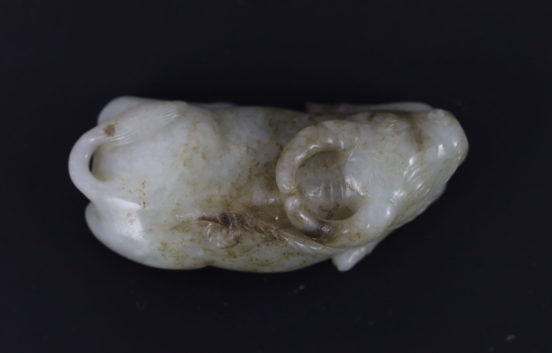 A Chinese Ming pale celadon and brown jade figure of a recumbent Buffalo, 16th/17th century, 8cm long